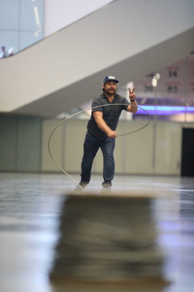 A man shows a peace sign while expertly whipping galvanized steel aircraft cable during the Harnessing ACCT showdown hosted at the 2025 conference and exposition in the Exhibit Hall.