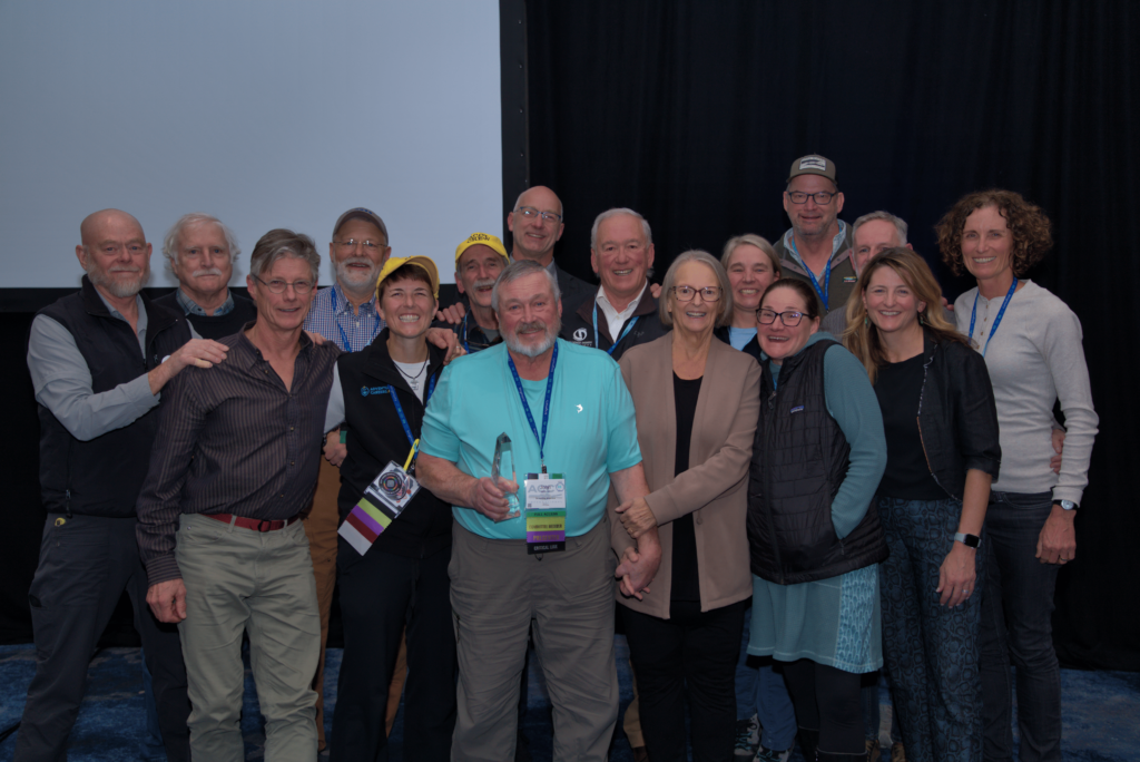 John Winter, the winner of the Critical Link award, holds his award while taking a group photo with all of the past recipients of the award after the Awards Ceremony at the 2025 ACCT conference and exposition.