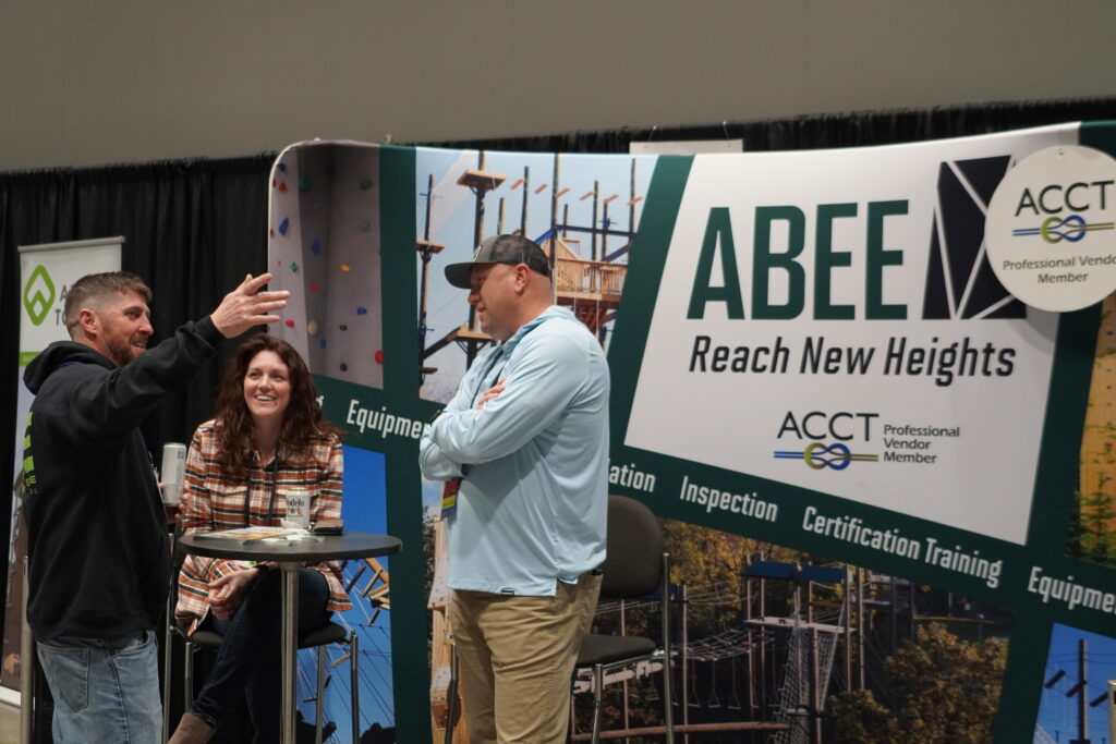 An attendee tells a story while two exhibitors smile as they listen in the Exhibit Hall.