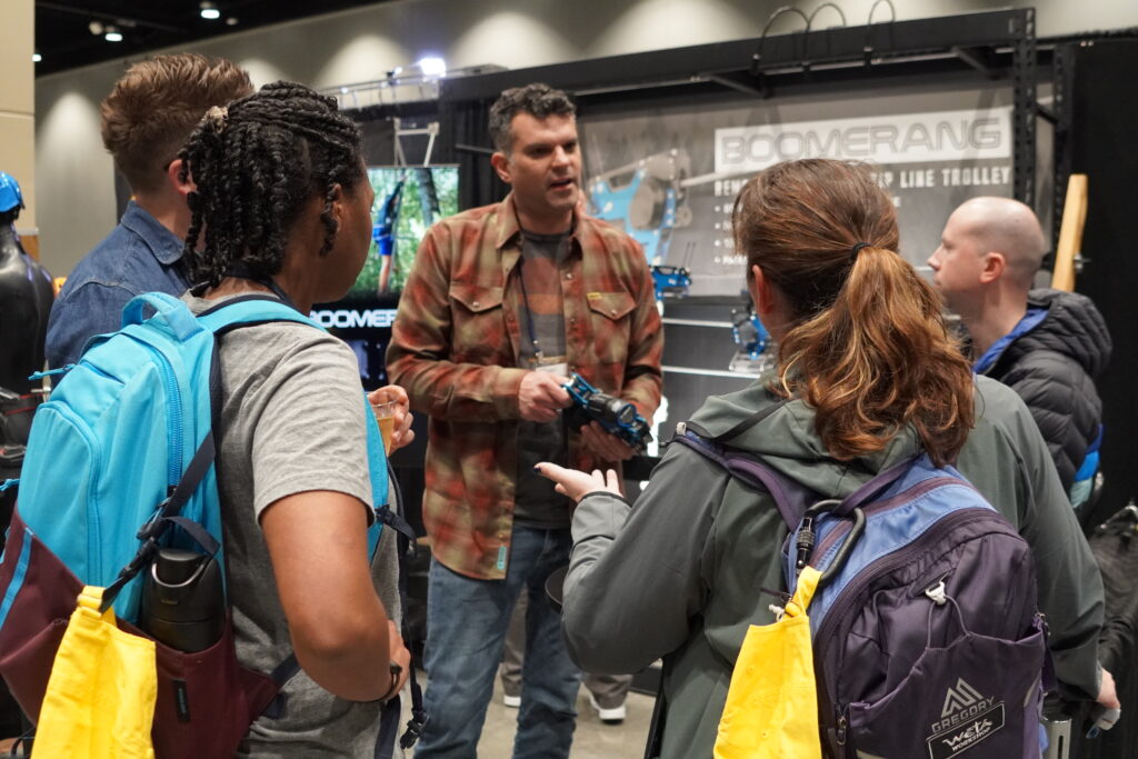 A group of attendees discuss a piece of equipment with an exhibitor in the Exhibit Hall.