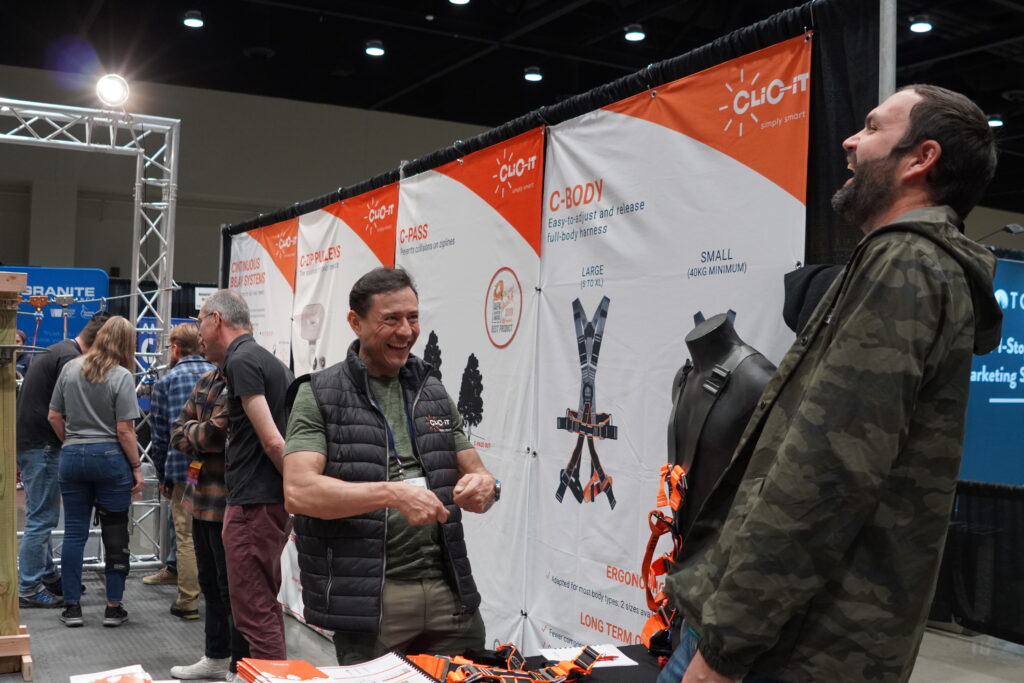 An exhibitor and an attendee laugh together while discussing gear in the Exhibit Hall.