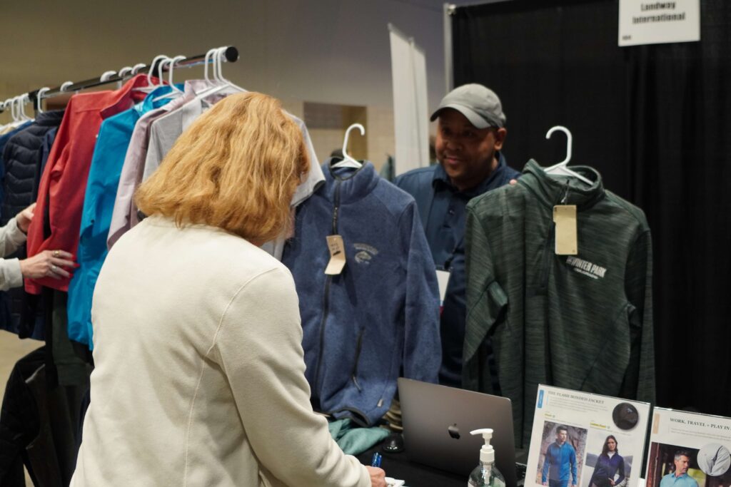 An exhibitor shares two branded jacket options with an attendee in the Exhibit Hall.