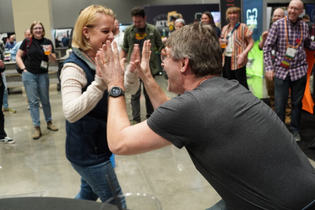 A man offers a woman an energetic high five after she succeeds during an impromptu challenge that popped up in the Exhibit Hall in 2024.