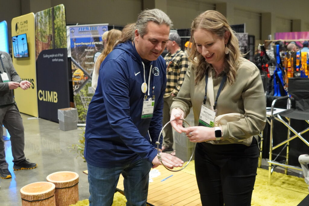 A man just passed off a buzz ring to a woman who smiles as she takes on the challenge of keeping the rings spinning in the ACCT Booth in the Exhibit Hall.