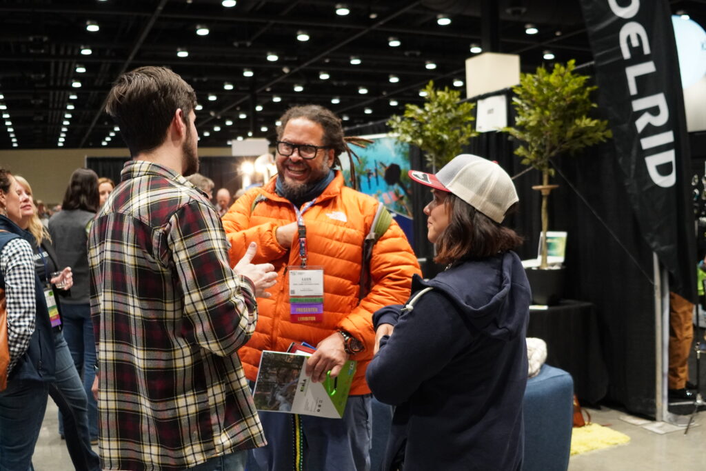 Three people smile and laugh together while chatting in the Exhibit Hall.