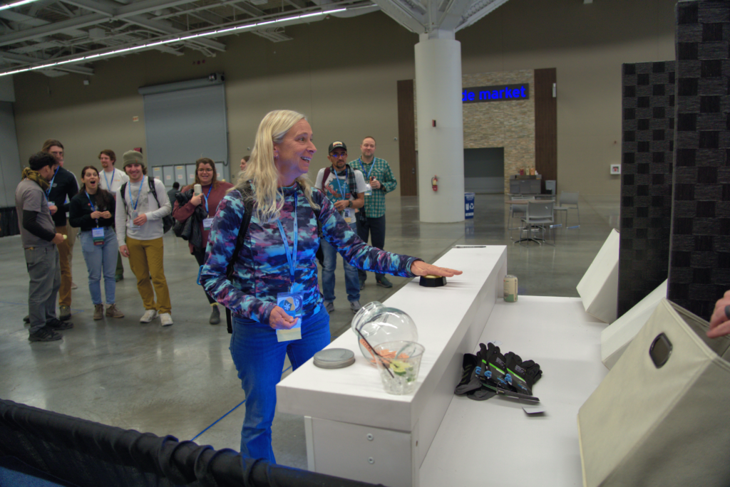 A hopeful winner hits the button for a chance to spin and win at the human slot machine at the ACCT booth in the Exhibit Hall while a crowd watches to see what happens during the 2025 conference and exposition.