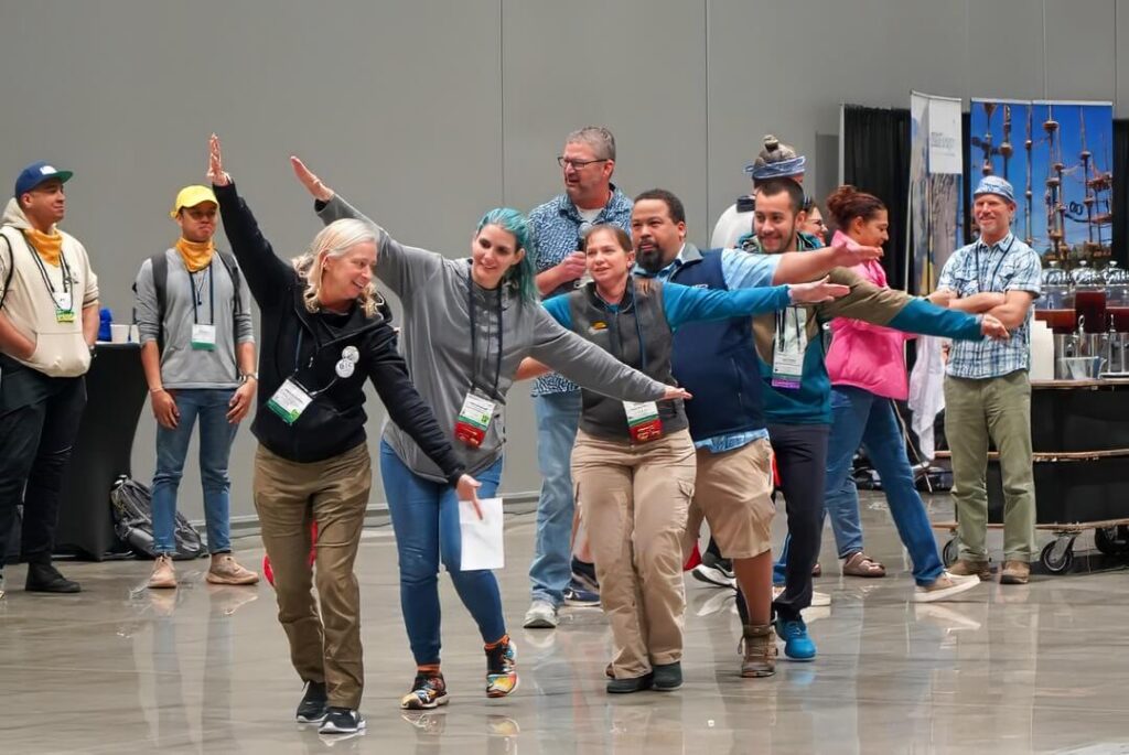 A team of people laugh and smile as they walk in a line with their arms outstretched, representing the red-tailed hawk that their team is named after.