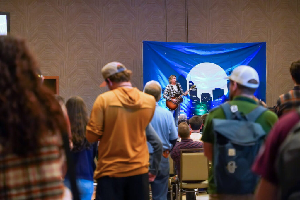 A room full of people watch a live performer on the main stage during the 2024 Opening Ceremony.