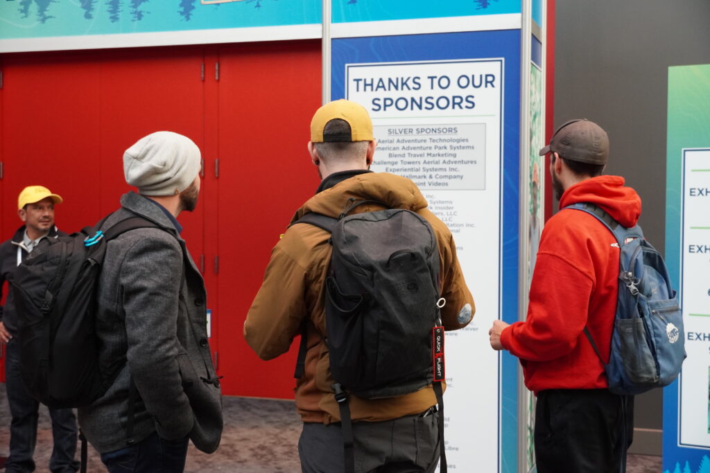 Three attendees examine a list of event sponsors as they wait for the Exhibit Hall to open.