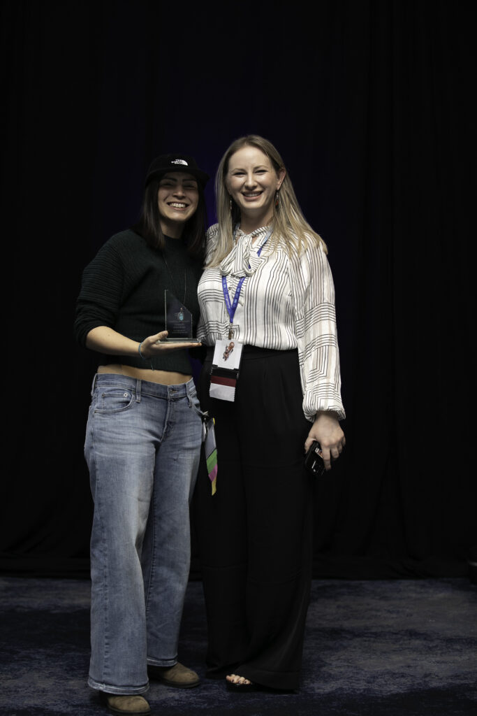 Annika Spriggs holds a Community Service Award while hugging ACCT Staff member Brittany Humphrey, who recognized Annika during the Awards Ceremony at the 2025 conference and exposition.