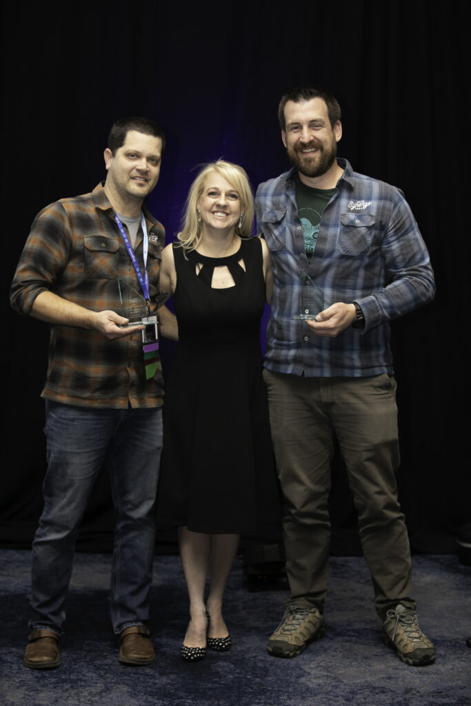 Alex Moore and Jason Marker hold their awards with Heather Brooks, who recognized the two with a Community Service Award during the Awards Ceremony at the 2025 ACCT conference and exposition.