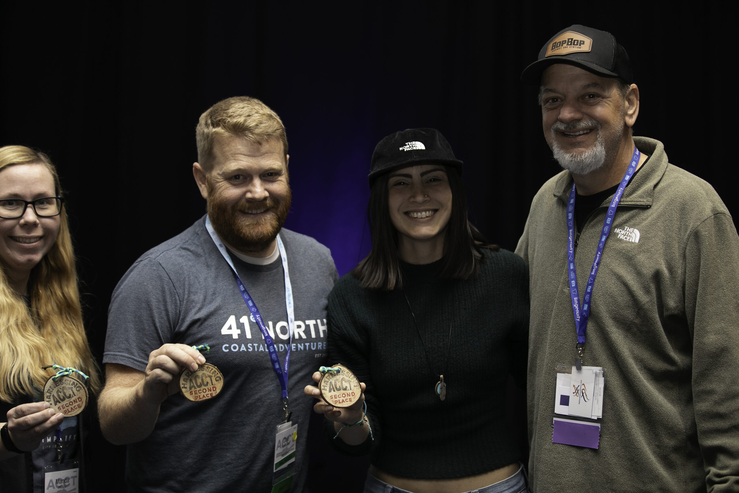 Four members of the Red Feather Flyers smile together while three members hold wood cookies that read "Harnessing ACCT Second Place" during the Awards Ceremony at the 2025 conference and exposition.