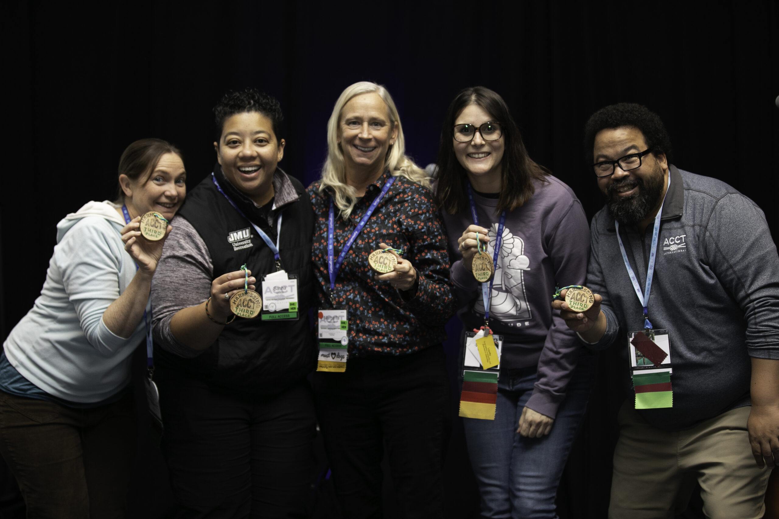 The five members of the Harnessing ACCT team Trillium Troublemakers hold wood cookies that read "Harnessing ACCT Third Place" stamped in black and red ink during the Awards Ceremony at the conference and exposition in 2025.