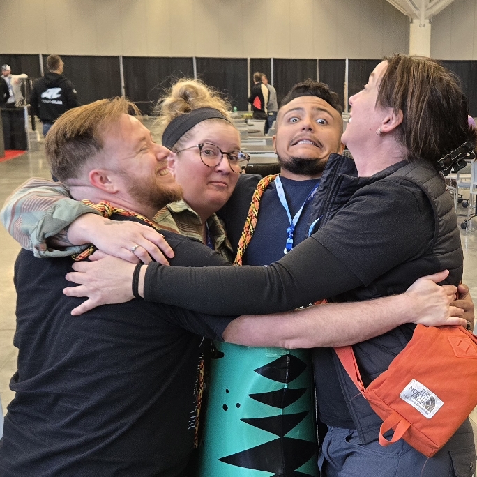 Four members of the Harnessing ACCT team Buckeye Treehuggers give one another a group hug in the Exhibit Hall during the 2025 conference and exposition.