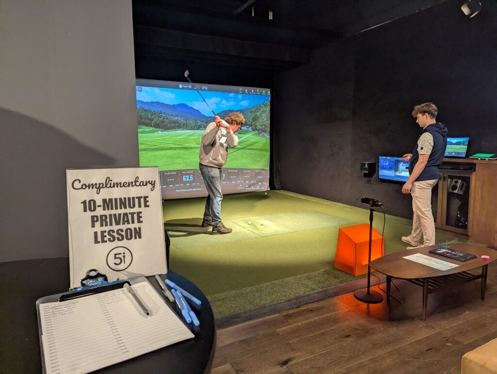 A man receives a complimentary 10-minute private lesson using a golf simulator at Five Iron Golf sponsored by Granite Insurance during the 2025 ACCT conference and exposition.