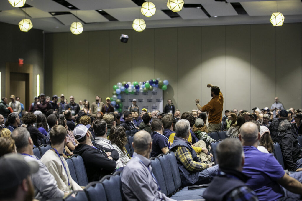 A man has just thrown a throwable microphone across the room as the mic sails to the intended user amongst the crowd of attendees of the Opening Ceremony during the 2025 conference and exposition.