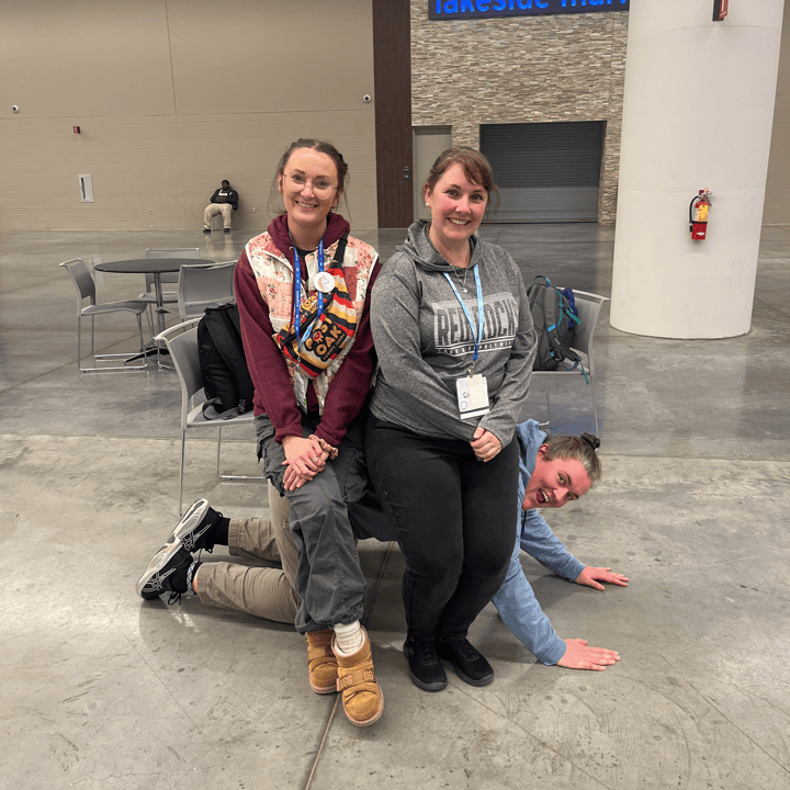 Two members of the Harnessing ACCT team Pawpaw Posse sit atop a third member of the team, who is pretending to be a park bench in the Exhibit Hall during the 2025 conference and exposition.