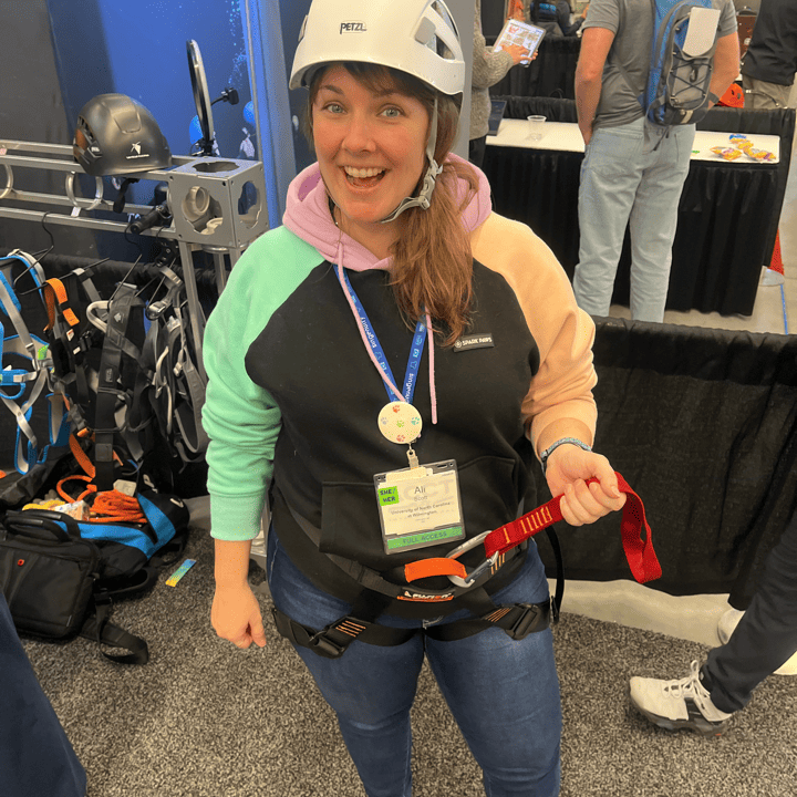 A member of the Harnessing ACCT team Pawpaw Posse smiles at the camera while wearing three pieces of personal protective equipment in the Exhibit Hall during the 2025 conference and exposition.