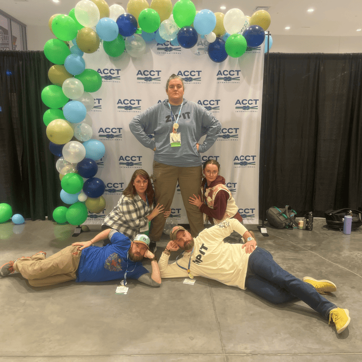 Five members of the Harnessing ACCT team Pawpaw Posse pose like an awkward '80s photo in front of the ACCT International balloon arch in the Exhibit Hall during the 2025 conference and exposition.