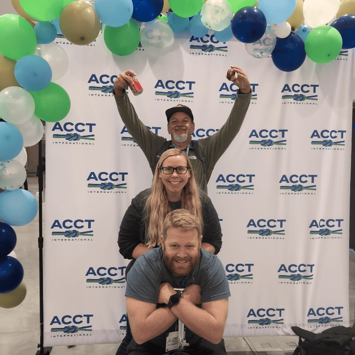 Three members of the Harnessing ACCT team Red Feather Flyers pose like an awkward '80s photo in front of the ACCT International balloon arch in the Exhibit Hall during the 2025 conference and exposition.