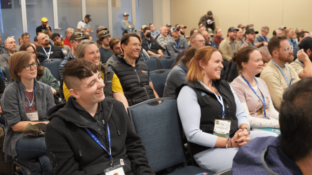 A crowd of session attendees sitting in chairs laugh and smile after hearing a joke during the 2025 ACCT conference and exposition.