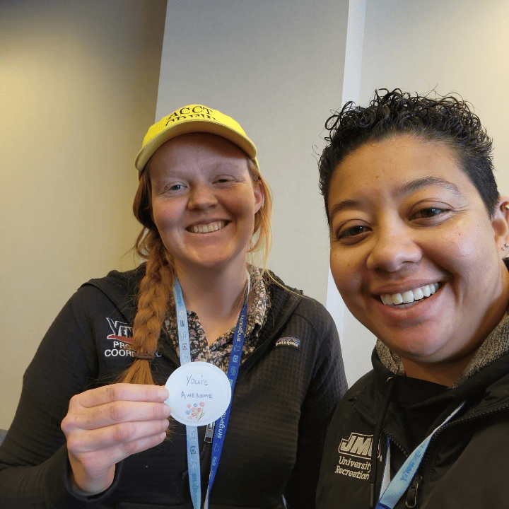 A member of the Harnessing ACCT team Trillium Troublemakers gives a button that reads "You're awesome" with a bouquet of flowers drawn underneath to a member of the Service Crew during the 2025 conference and exposition.