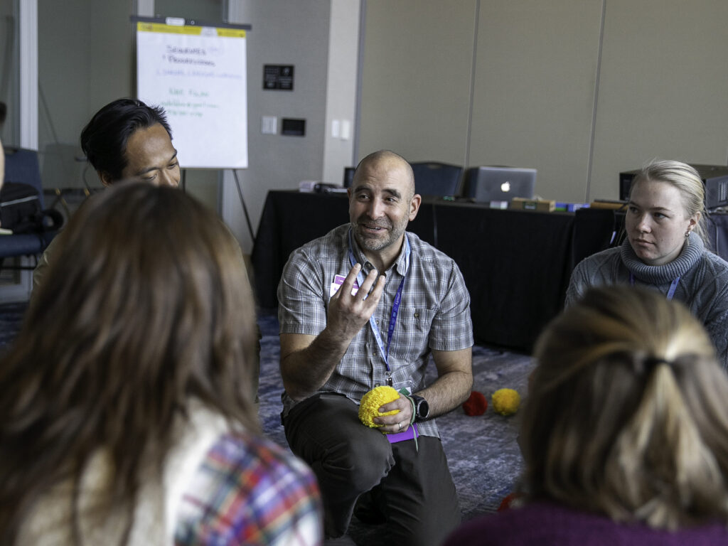 A presenter debriefs an activity with attendees while sitting or kneeling on the floor during the 2025 ACCT conference and exposition.