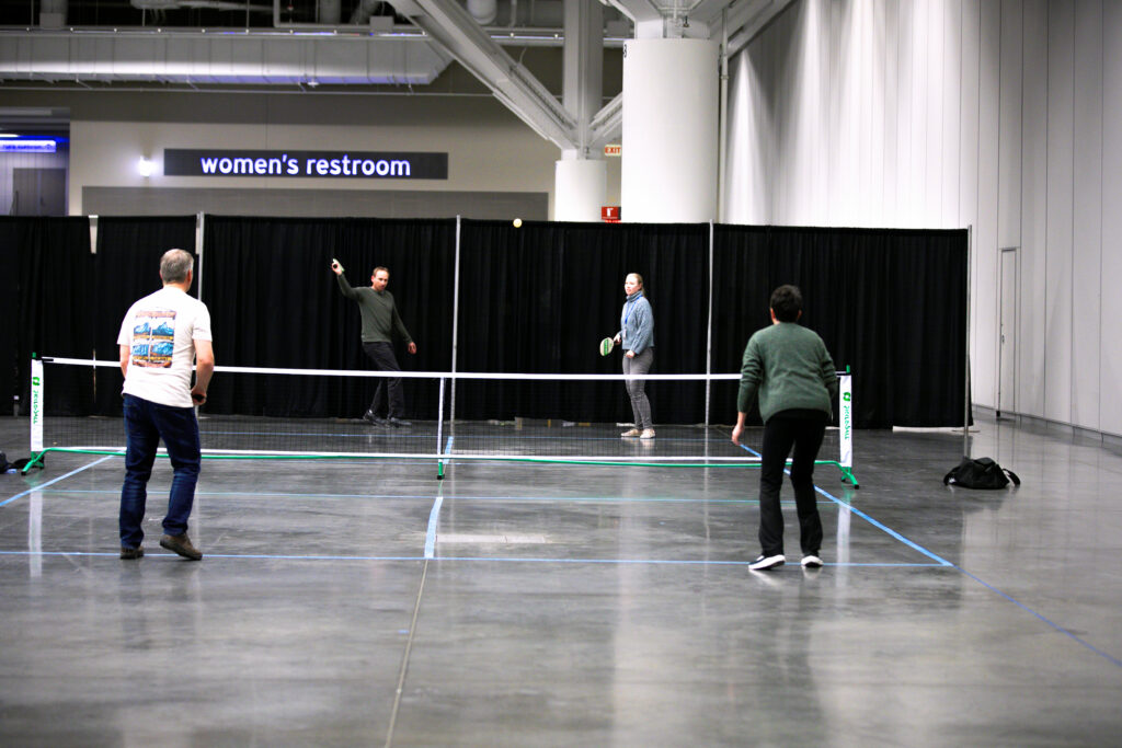 Four people play pickleball, loaned by the Cuyahoga Community College for the 2025 conference and exposition, in the Exhibit Hall.