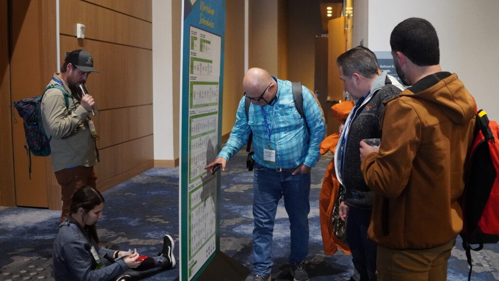 Five attendees review the big grid of Workshop Schedules between sessions in the host hotel at the 2025 ACCT conference and exposition.