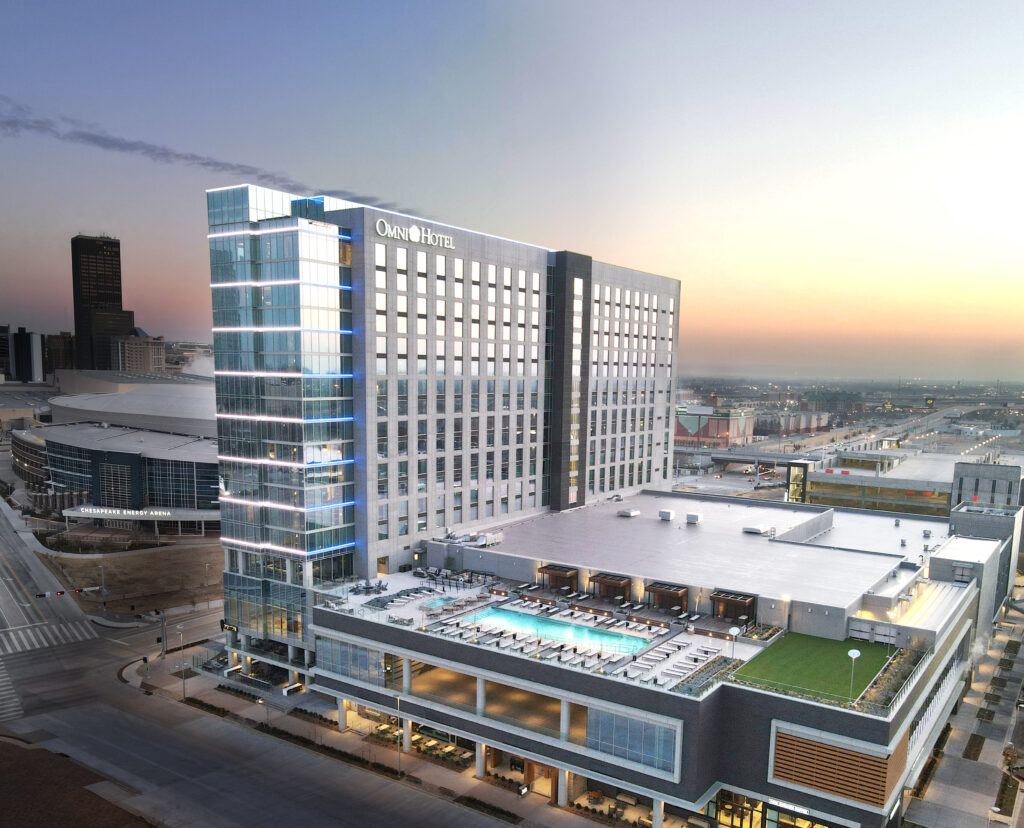 The hotel and outdoor pool deck of the Omni Oklahoma City Hotel in Oklahoma is seen in the light of sunset.